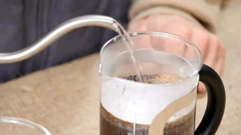 Pouring Coffee Grounds And Hot Water Into The French Press